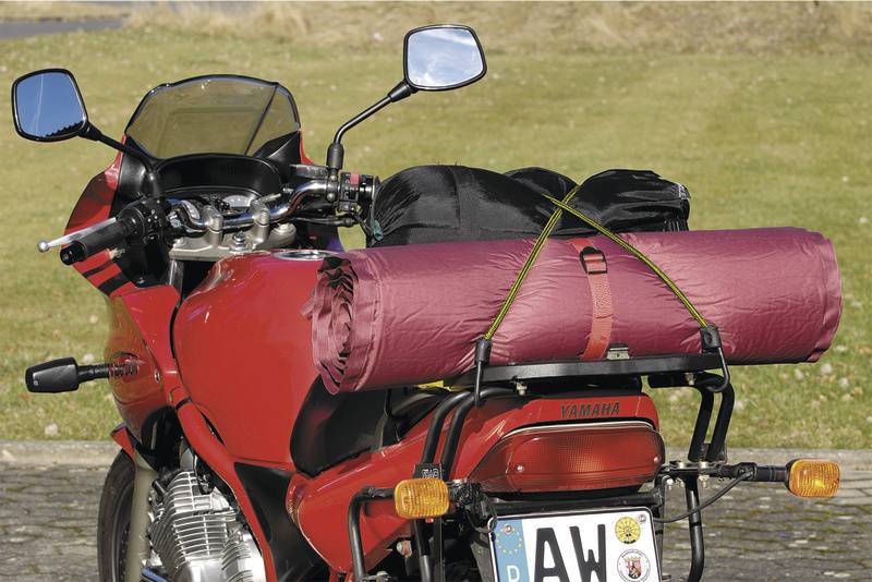 Červená motorka s stanom pripevneným na nosiči batožiny. Motorka stojí na vonkajšej spevnenej ploche.