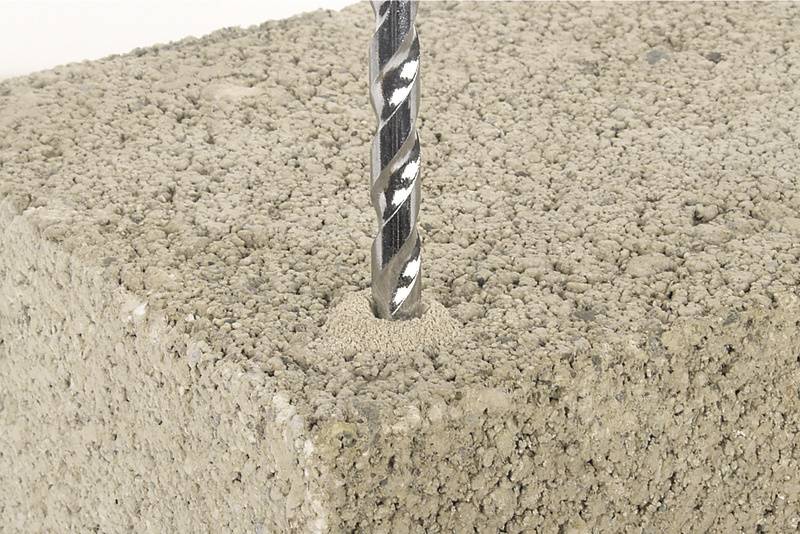 Vrták preniká do pórovitého betónového bloku. Detailný záber ukazuje proces vŕtania a štruktúru stavebného materiálu.