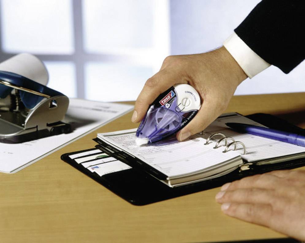 Osoba opravuje ručne písané poznámky v organizátore. V pozadí je vidieť dierkovač.