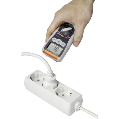 Ruka drží multimeter, ktorý meria napätie v zásuvke pripojnej do rozvodnej lišty. Na displeji je zobrazená hodnota '70'.