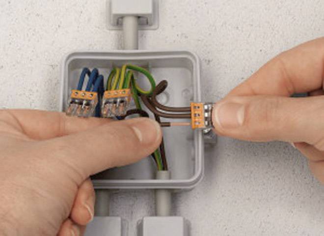 Osoba pripája káble v sivej zásuvke. Viacfarebné káble sú prepojené konektormi.