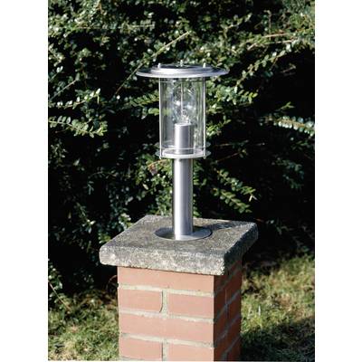 Strieborná záhradná lampa na murovanom podstavci pred pozadím zelených listov.