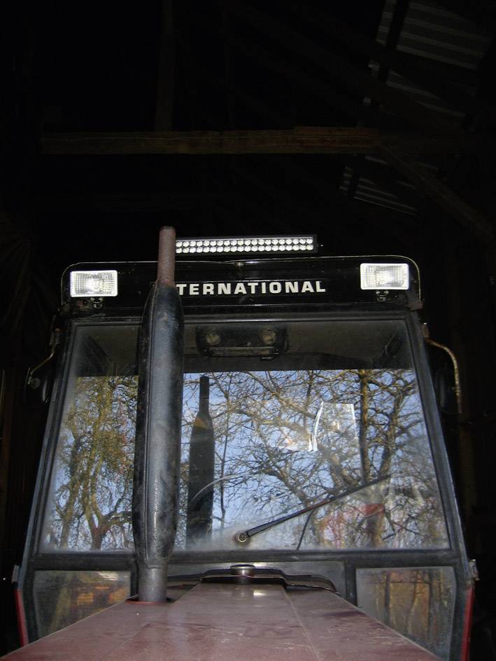 Pohľad spredu na traktor s nápisom 'INTERNATIONAL' nad čelným sklom, stromy odrážajúce sa v skle.