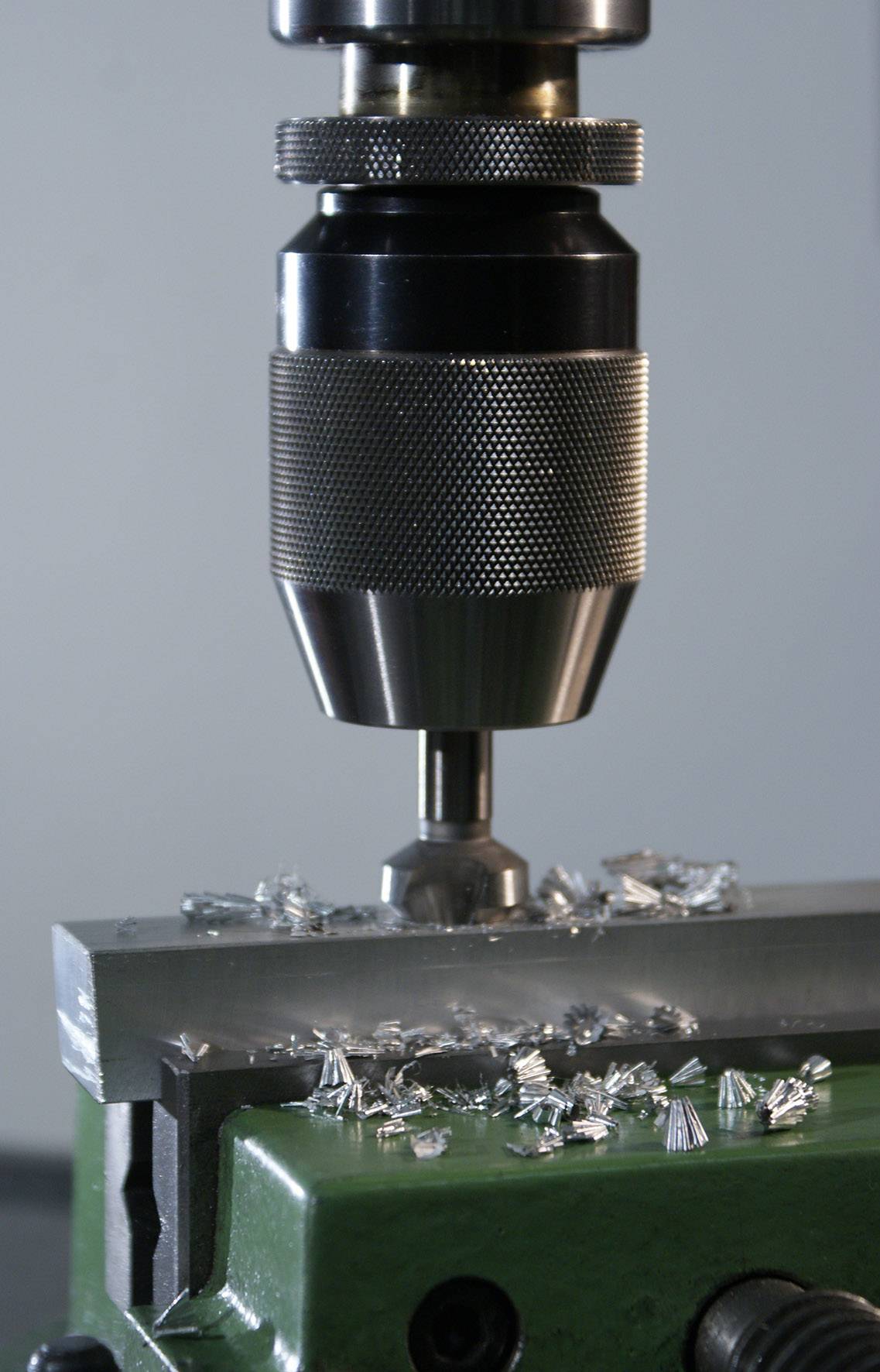 Vŕtačka opracúva kov v dielni. Kovové triesky sú viditeľné okolo vyvŕtaného otvoru.