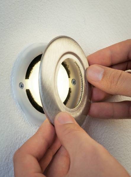 Osoba používa obe ruky na otvorenie alebo zatvorenie okrúhleho vetráckeho krytu, ktorý je namontovaný v stene.