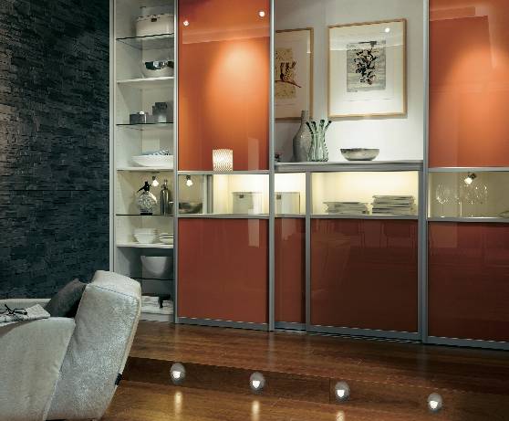 Obrázok zobrazuje štýlovú obývaciu izbu s modernými nábytkom a dekoratívnou stenou plnou políc. V popredí stojí kreslo.