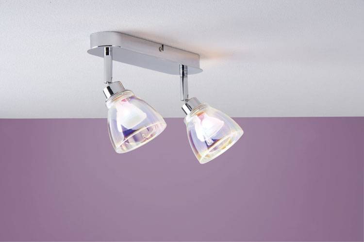 Dve nastaviteľné stropné svietidlá s priehľadným skleneným tienidlom na striebornom držiaku vyžarujú mäkké svetlo pred fialovou stenou.