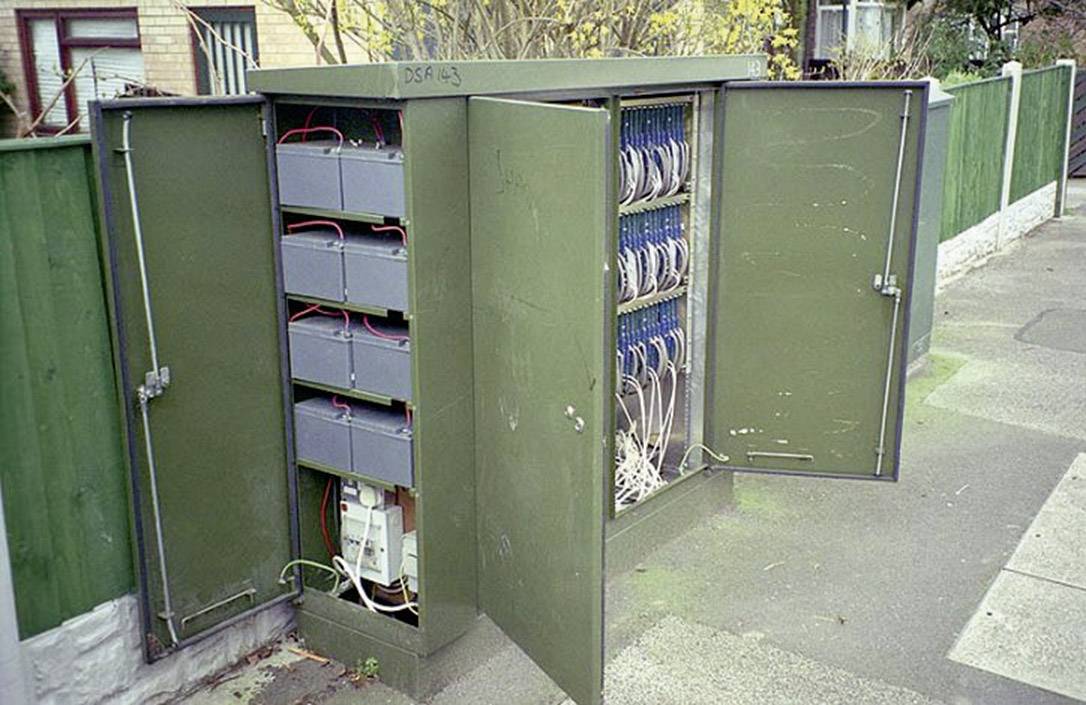 Otvorený, zelený telekomunikačný rozvádzač na chodníku odhaľuje vnútri káble a rôzne technické komponenty.