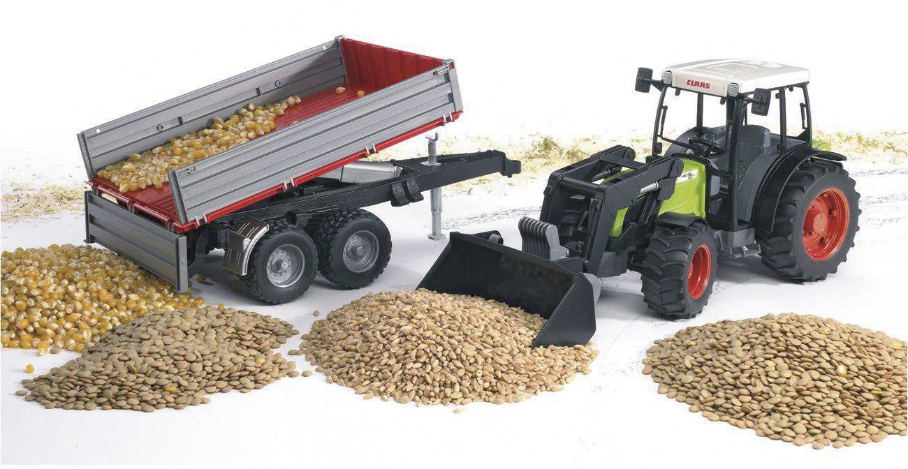 Traktor s prívesom vykladá obilie na zem. Je vidieť veľkú hromadu kukurice a iných zŕn.