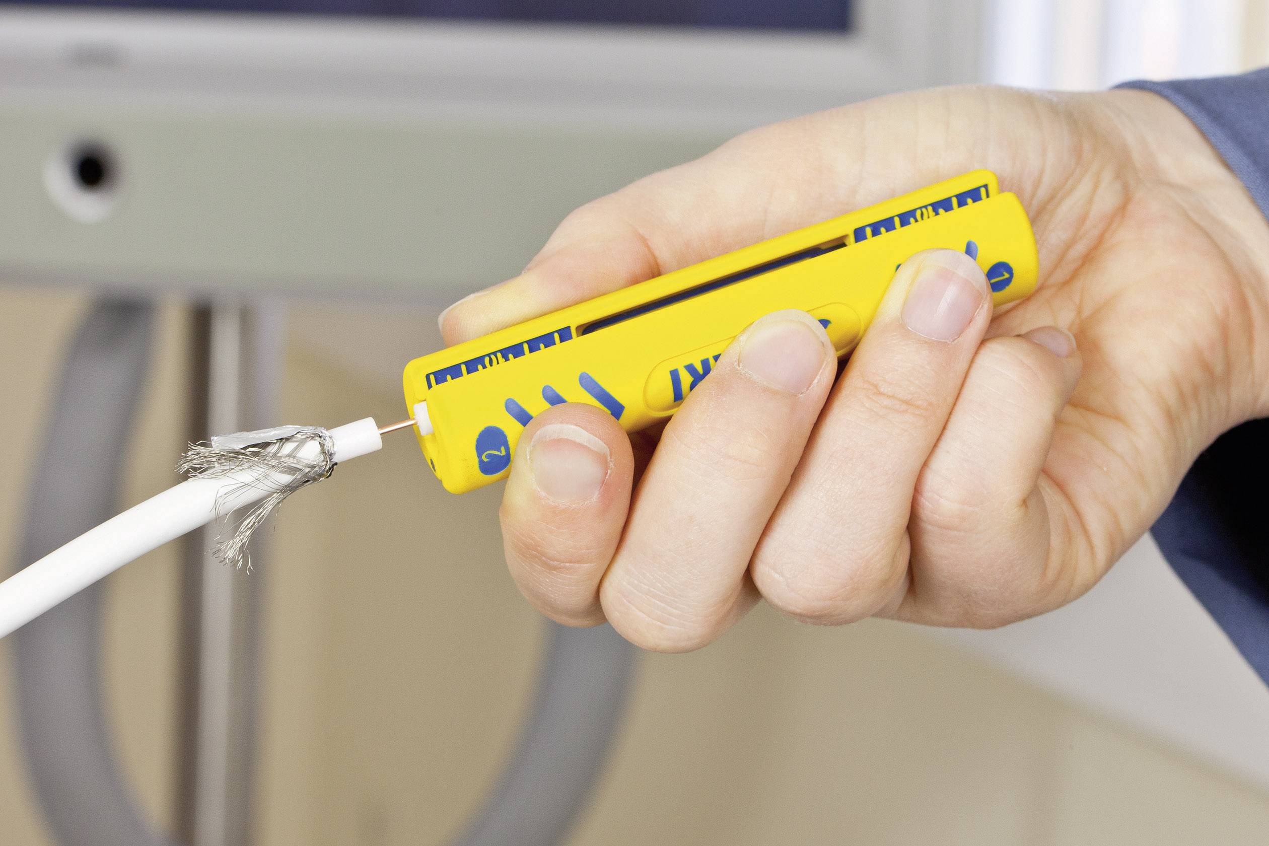 Jedna ruka drží žlté testovacie zariadenie káblov pri poškodenom elektrickom kábli. Kábel má odhalené vodiče, čo poukazuje na nebezpečenstvo.