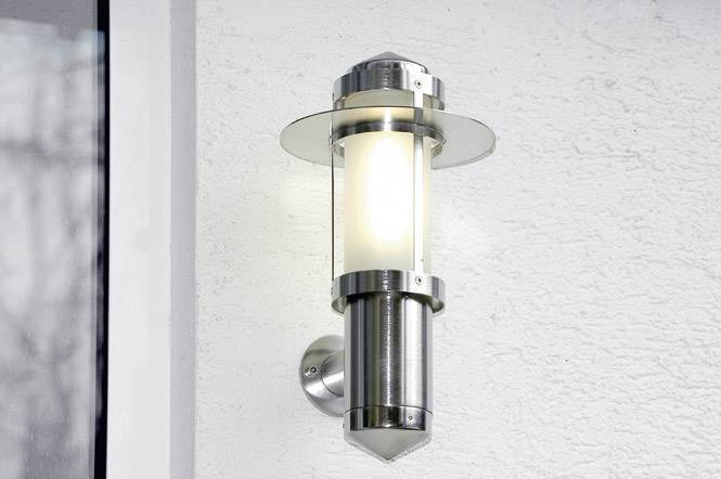 Strieborná nástenná lampa na bielej stene, zapnutá, vyžaruje teplé svetlo, moderný dizajn.