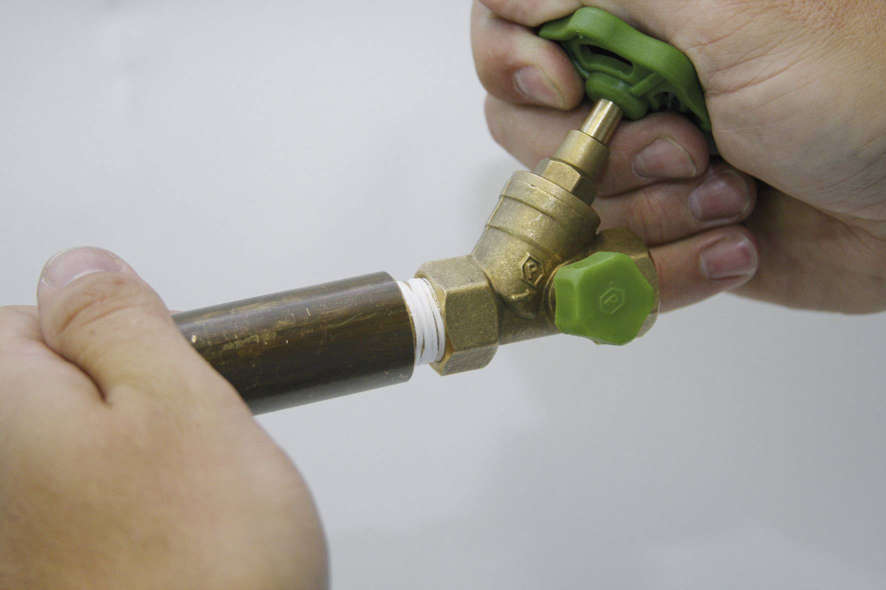 Osoba uťahuje ventil na medenej trubke so zeleným otočným ovládačom.