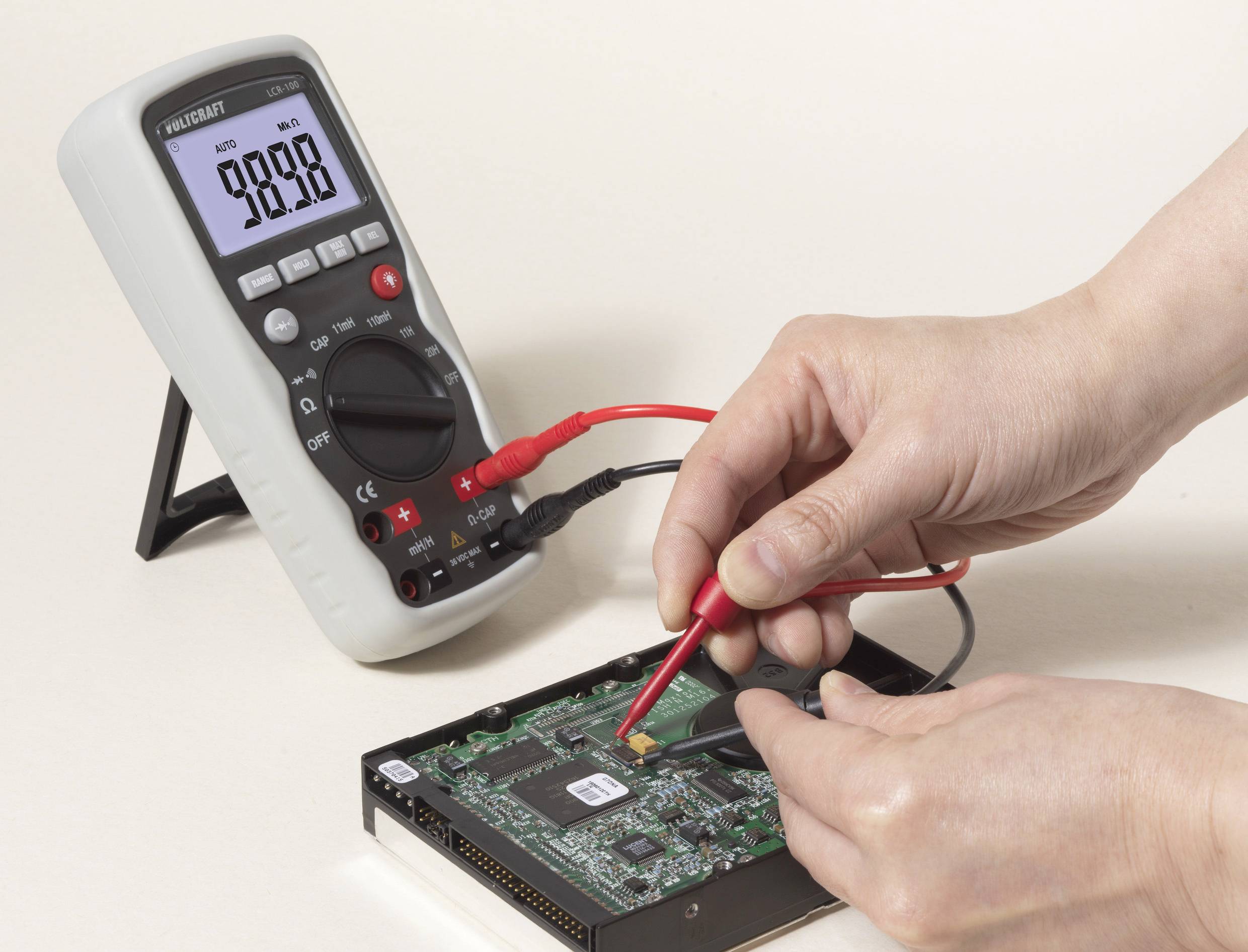 Nekdo z multimetrom meri napetost na računalniški plošči. Multimeter prikazuje 9,888 V.