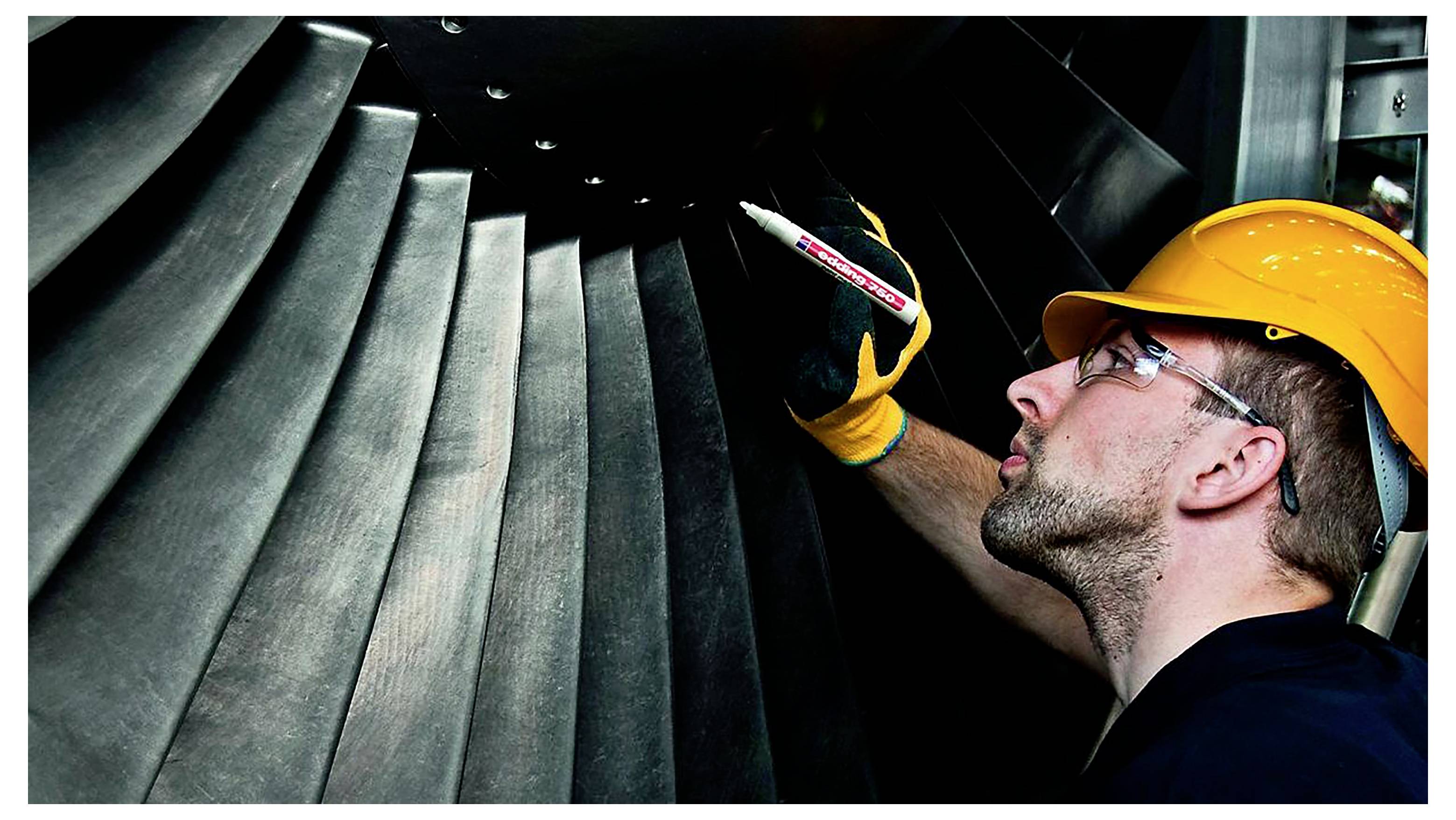 Inženir v varovalni čeladi pregleduje velike industrijske turbinske lopatice s prenosnim merilnikom znotraj ohišja stroja.