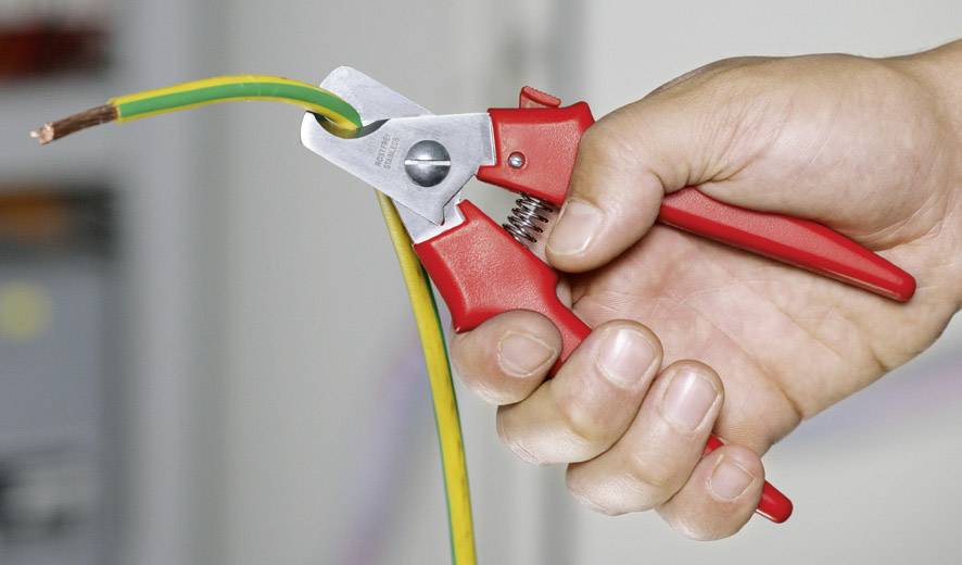 Ena roka drži rdečo kabelsko klešče in odstranjuje izolacijo z zelenega in rumenega električnega kabla.
