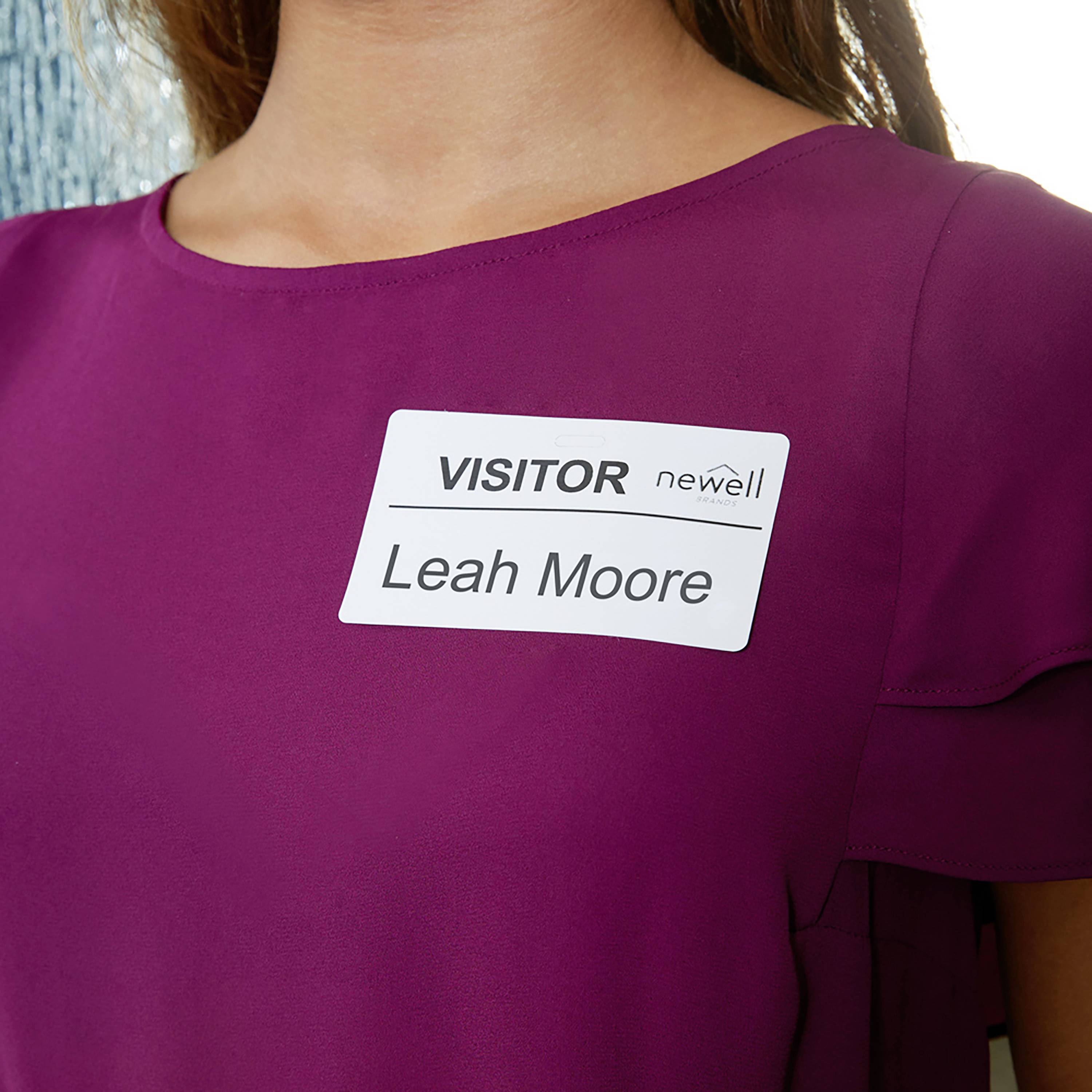 Oseba v vijolični zgornji oblačili nosi obiskovalsko priponko z imenom 'Leah Moore' in logotipom podjetja Newell.