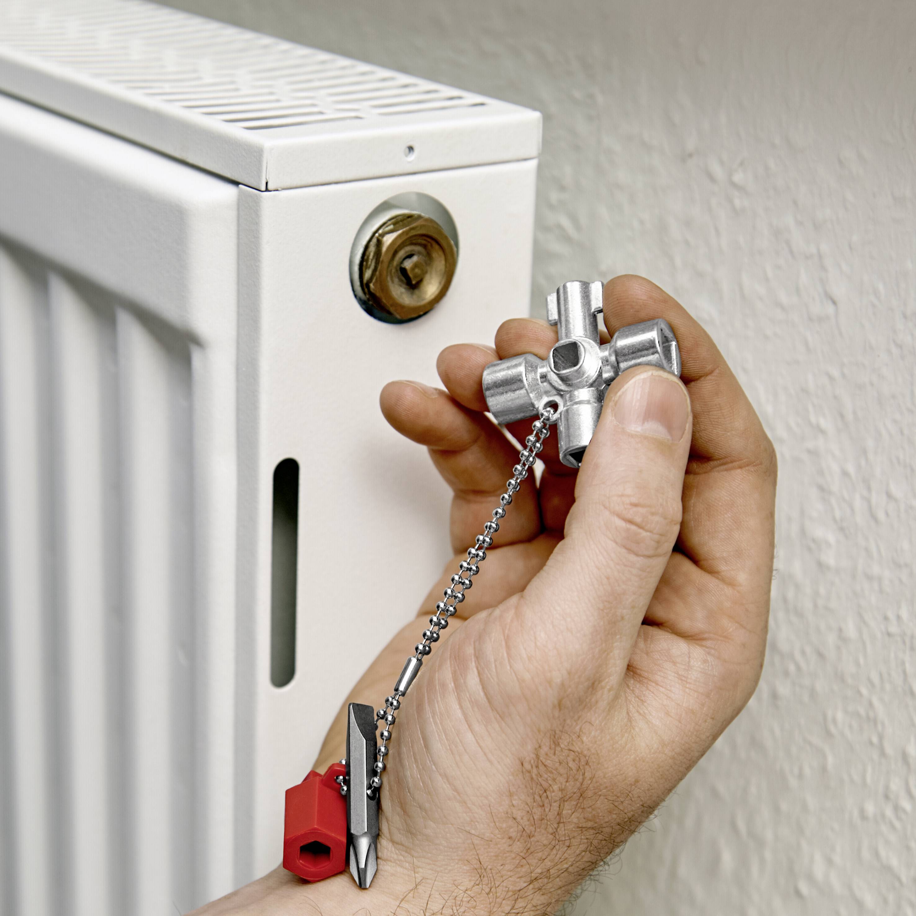 Ena roka drži odzračevalni ključ pred belim ventilom radiatorja, pripravljena za odzračevanje radiatorja.