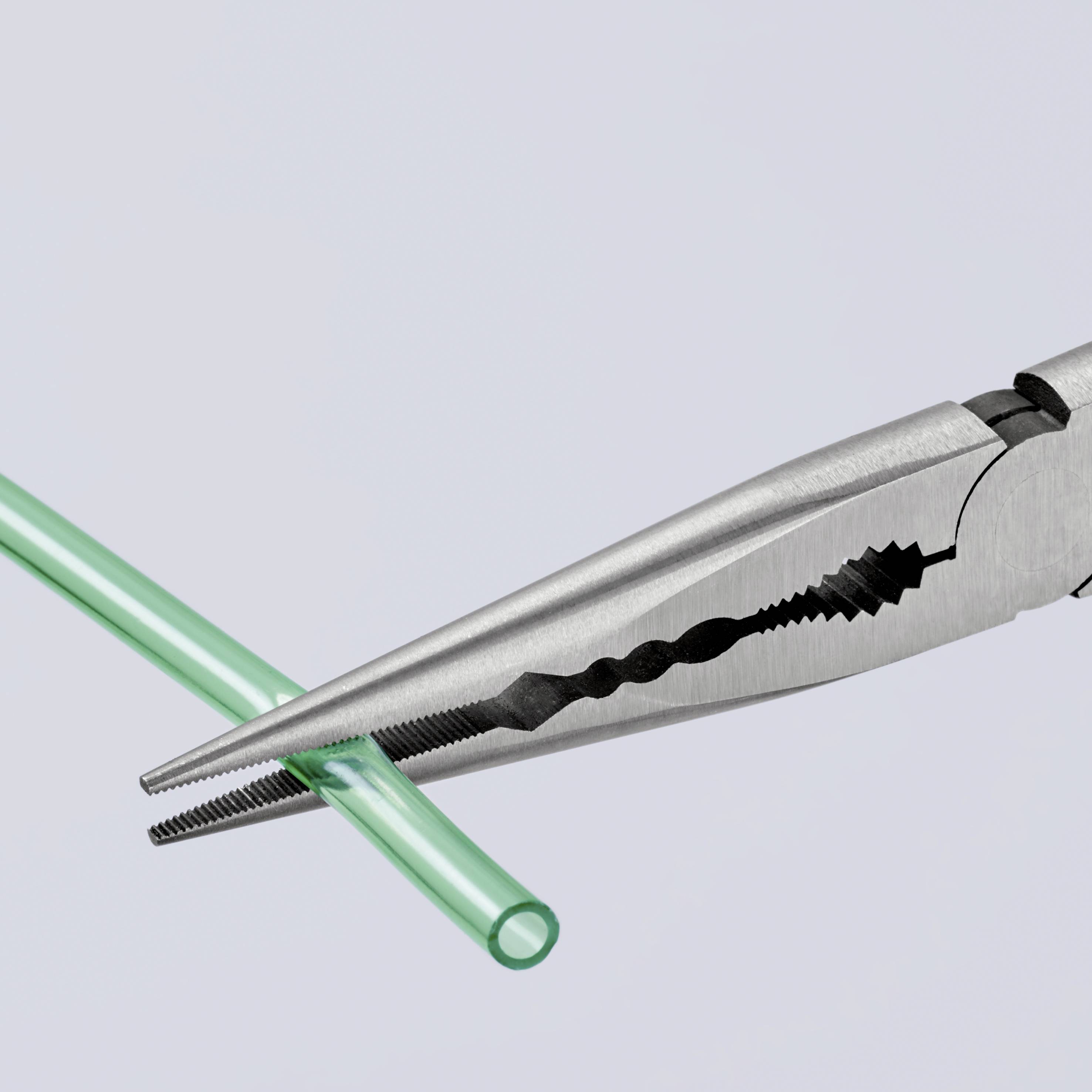Klešče sekajo zeleno plastično cev. Klešče so iz kovine in imajo nazobčane čeljusti, ki zagotavljajo natančnost.
