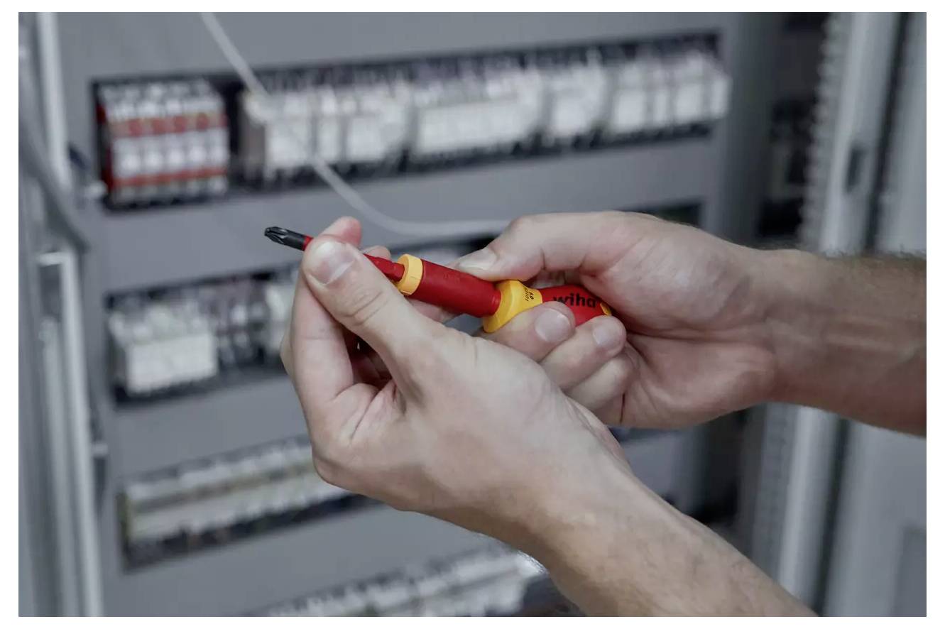 Oseba uporablja izolirano vijačnik za delo na električni plošči, pri čemer se osredotoča na varnost in natančnost.