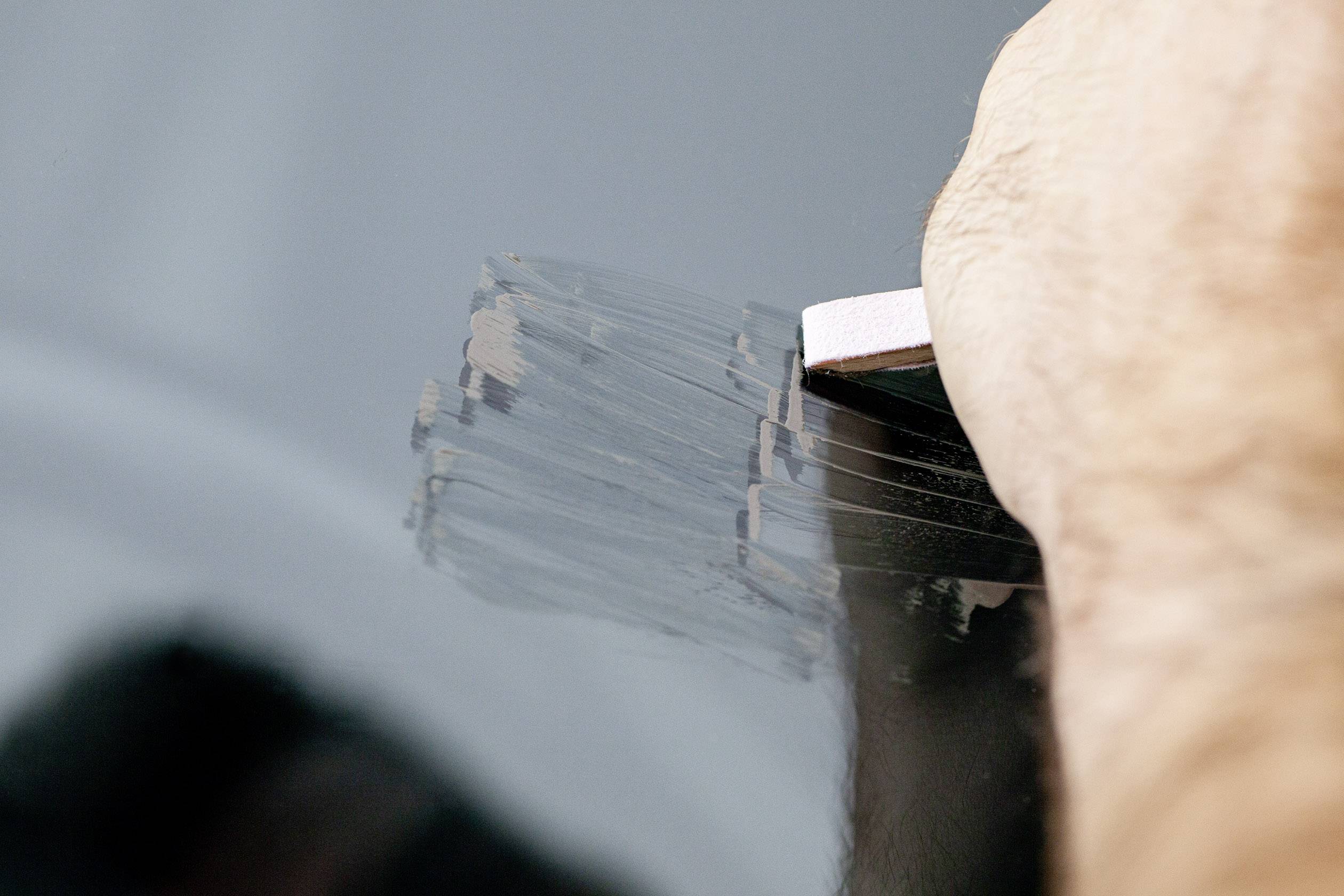 Ena roka drži radirko in briše sledi svinčnika na gladki, temni površini.