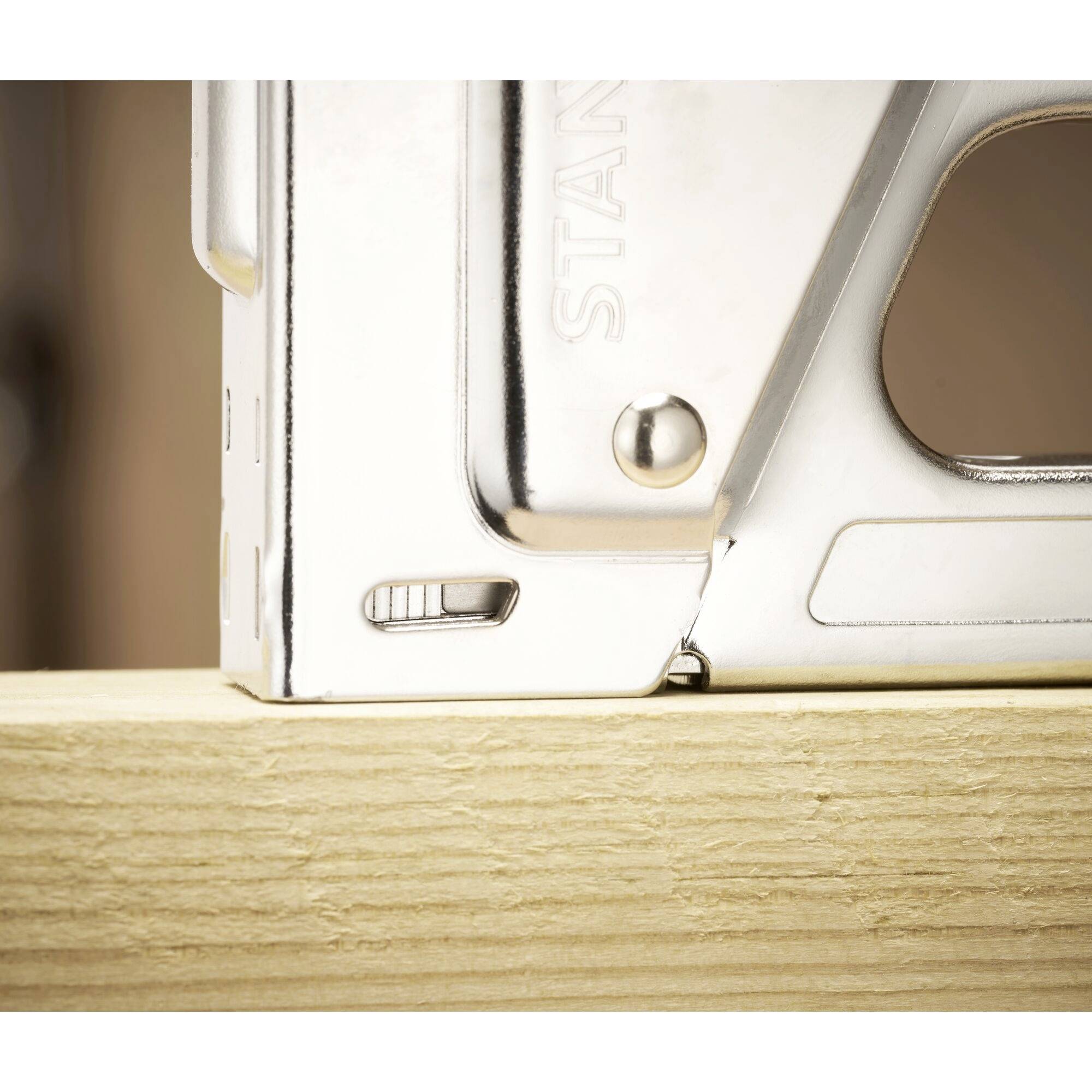 Na leseni mizi leži srebrn spenjalnik. Pozornost je usmerjena na kovinski sijaj in desni zgornji rob naprave.