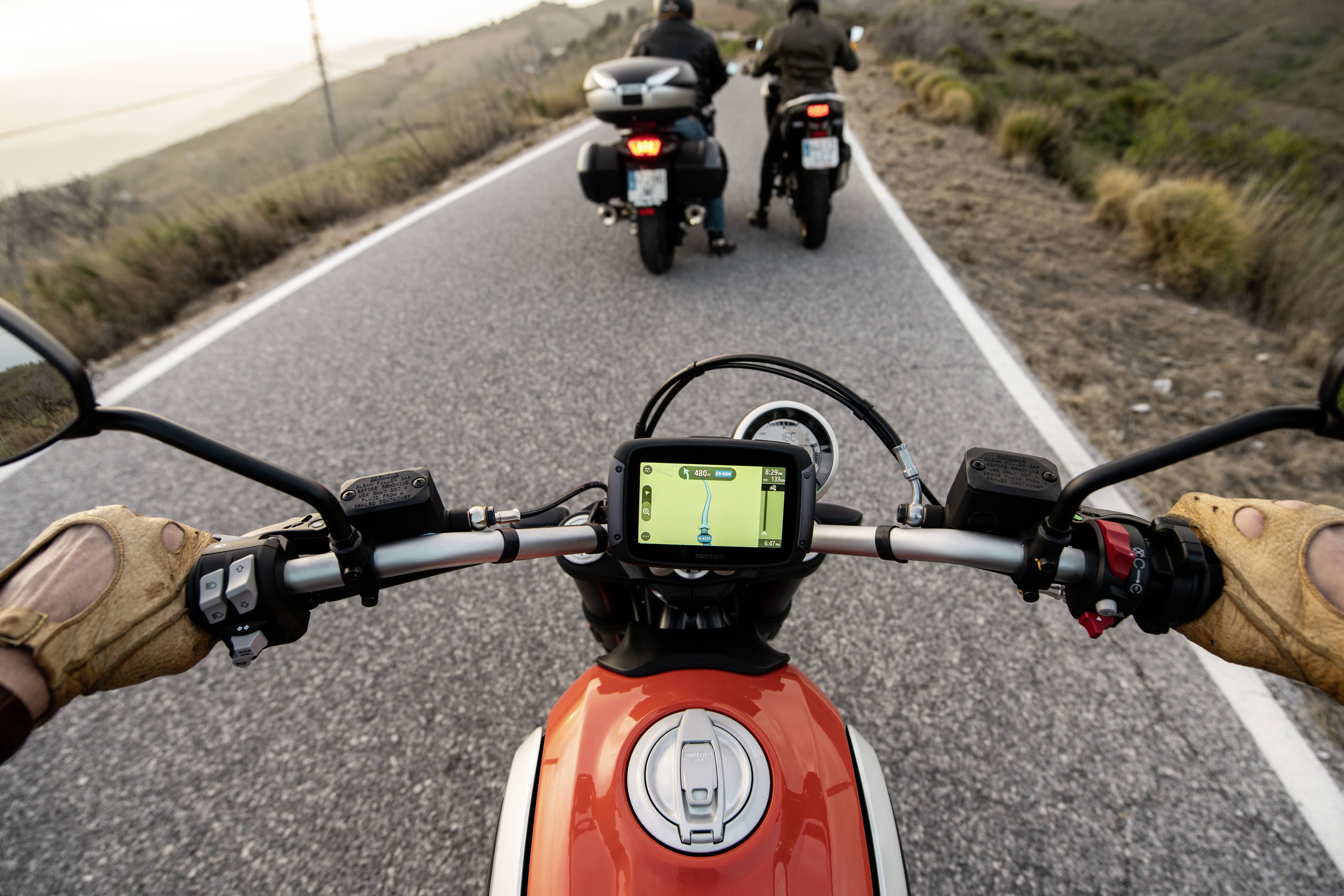 Pogled motorista na vijugasti cesti, ki sledi paru motokros voznikov. Navigacija GPS na zaslonu.
