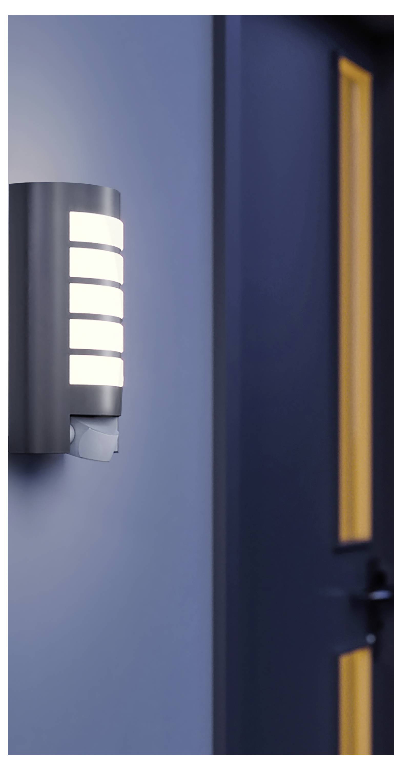 Stenska zunanja luč, ki sveti ob temno modri vrati z ozkim navpičnim oknom.