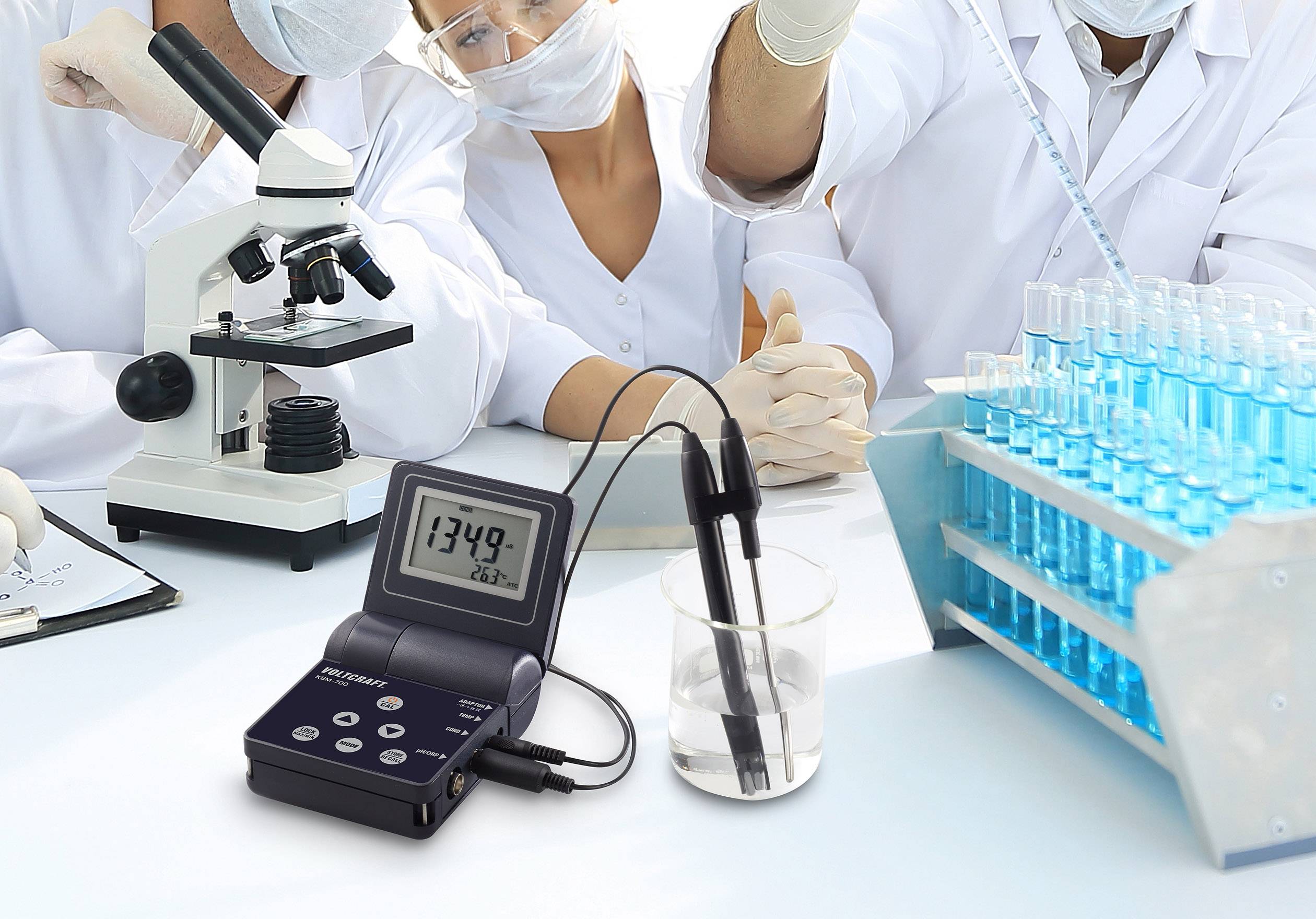 Znanstveniki delajo v laboratoriju z mikroskopi in preizkusnimi cevkami. V ospredju je pH-meter, ki prikazuje vrednost 13,49.