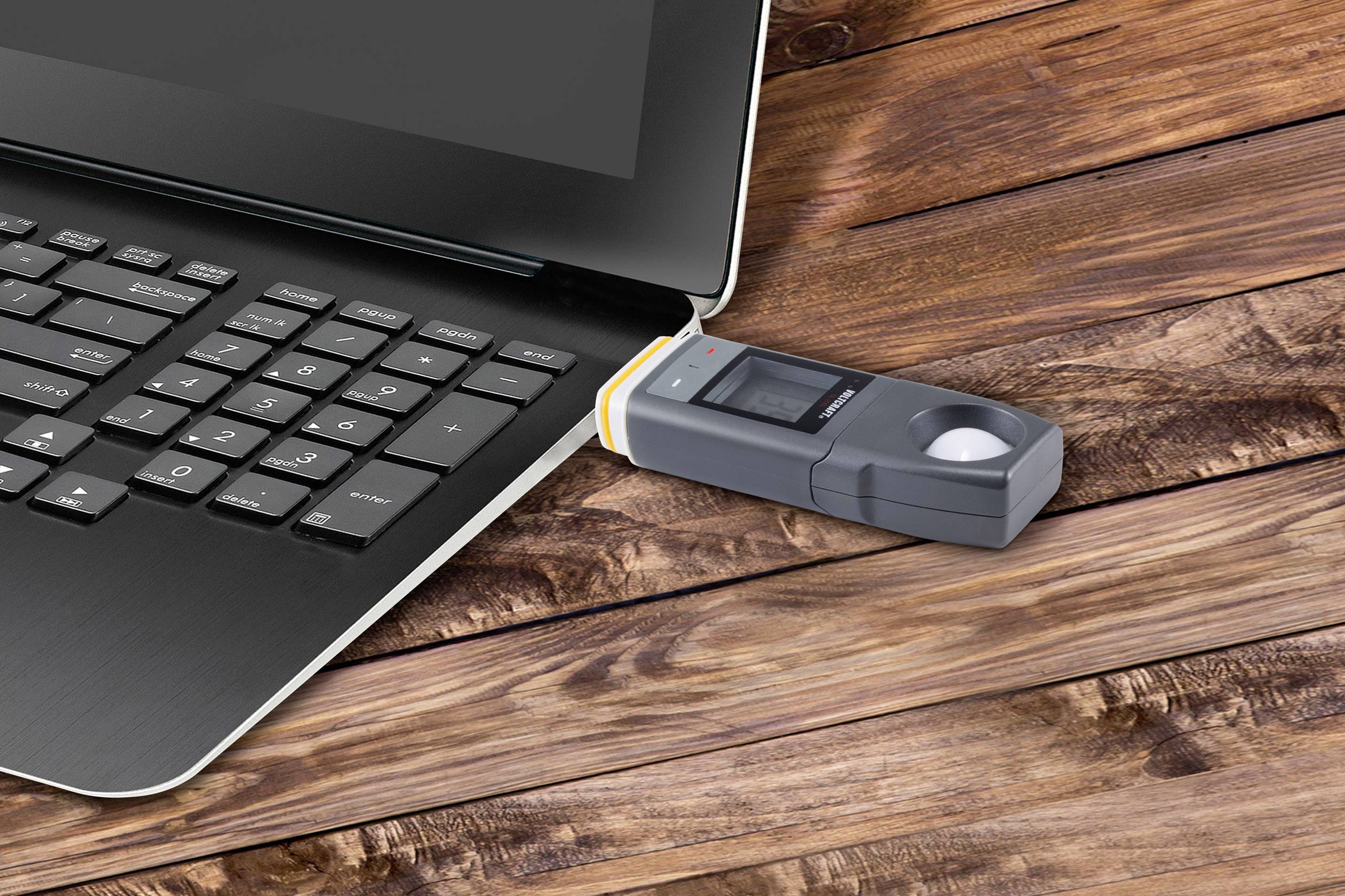 Prenosni računalnik z USB priklopljenim senzorjem prstnih odtisov na leseni mizi.