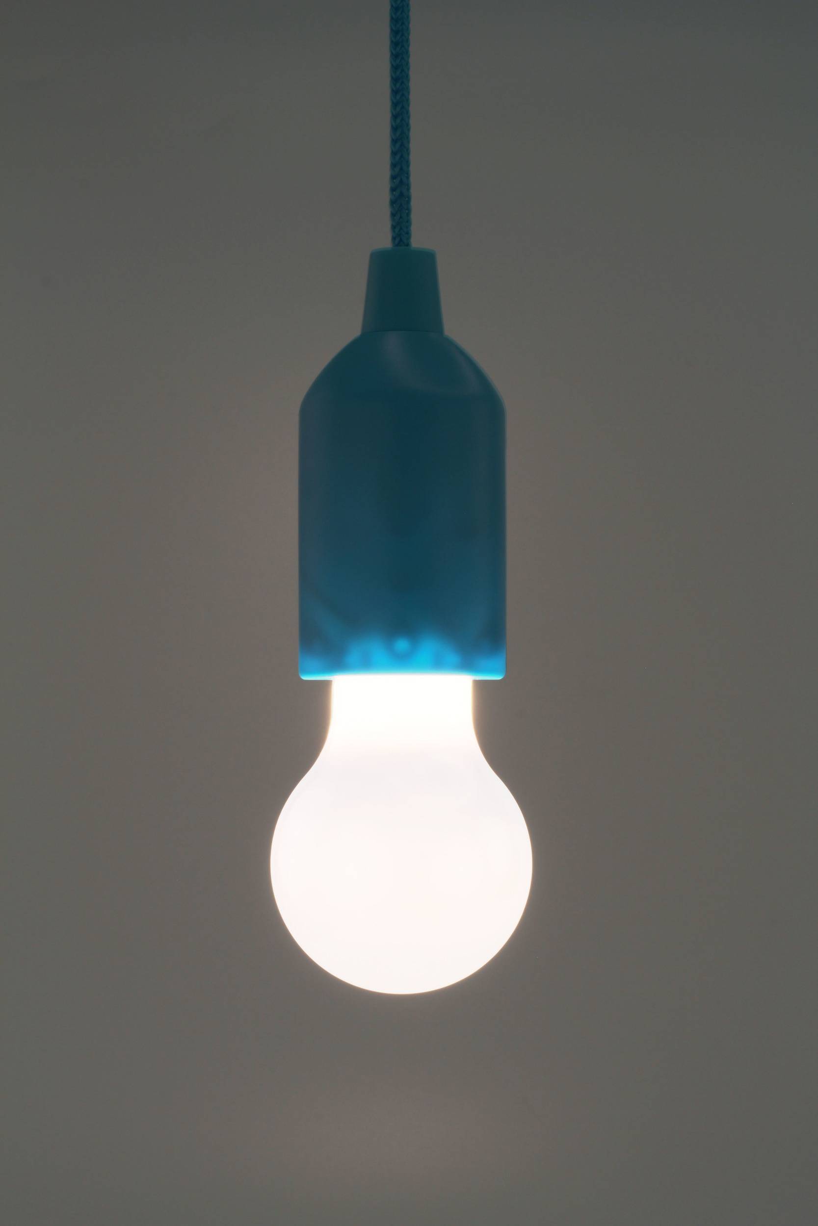 Žareča žarnica visi s stropa, obdana z mrakom, simbolizira inovacijo ali idejo.