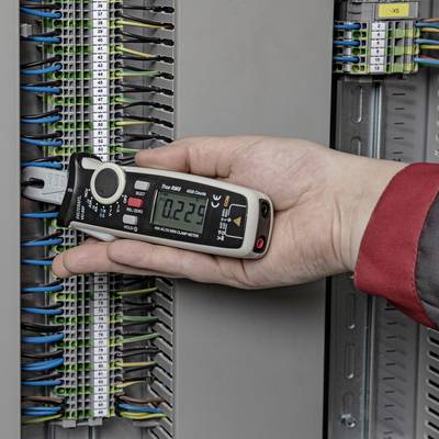 Roka drži multimeter, ki je priključen na odprto elektro omaro za merjenje električne napetosti.
