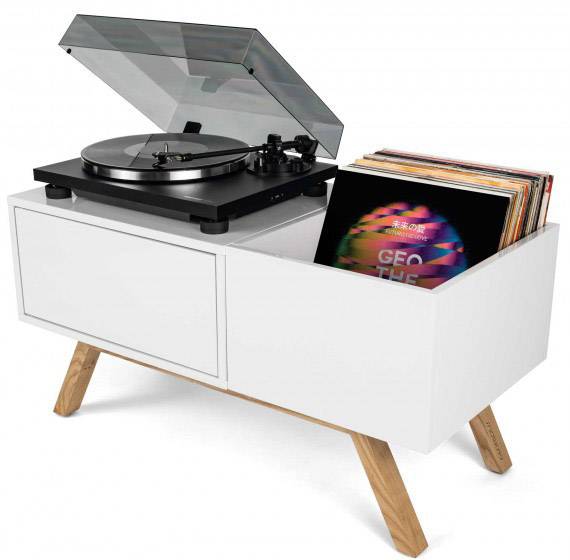Gramofon v sodobni beli omari z lesenimi nogami, ki predvaja vinilno ploščo. Desno so zložene dodatne plošče.
