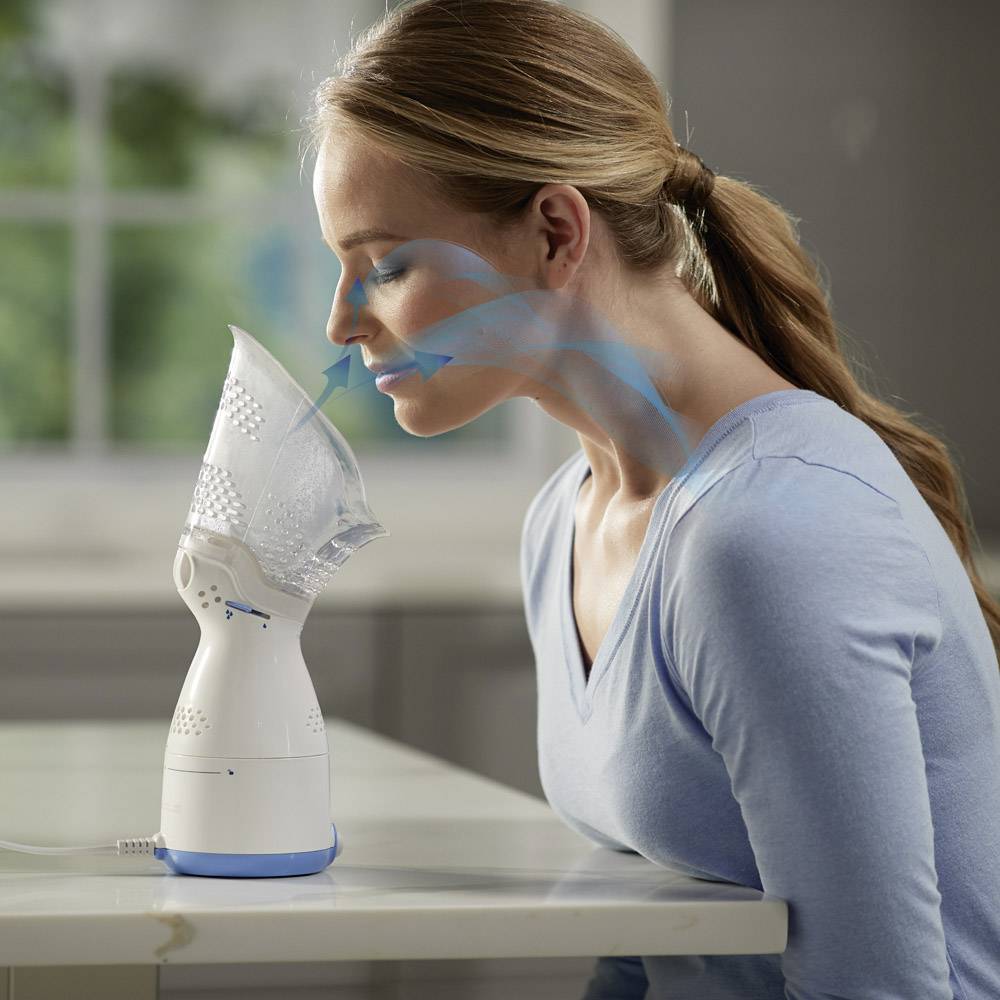 Ženska uporablja električni inhalator za zdravljenje dihalnih poti. Modra puščica kaže pot zraka od naprave do nosu.