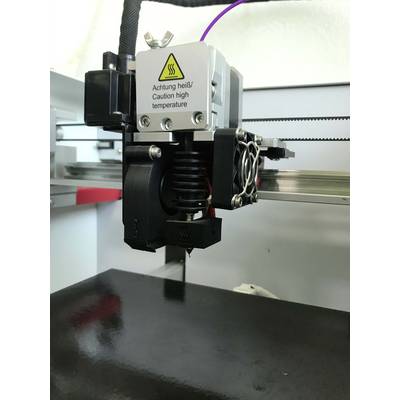 3D-tiskalnik z opozorilnim znakom 'Pozor vroče!/Previdno visoka temperatura'. Bližnji posnetek glave tiskalnika med delovanjem.