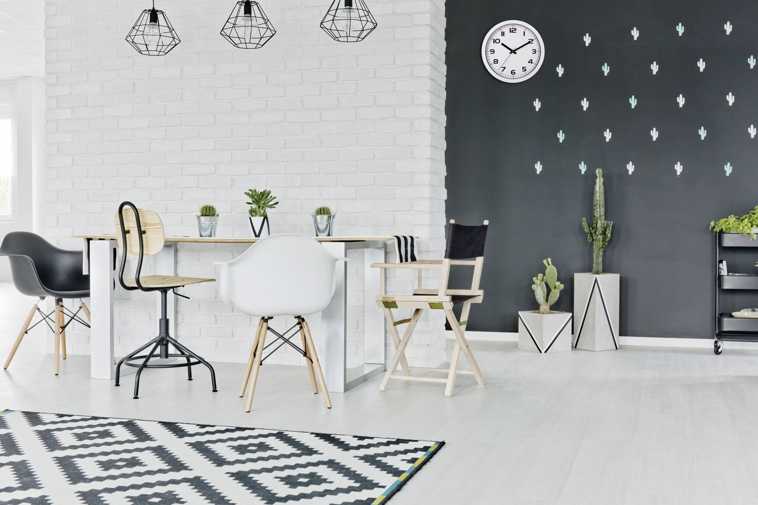 Sodoben prostor za bivanje s svetlim pohištvom, rastlinami in geometrijskim preprogom. Ura kaže približno 10:10.