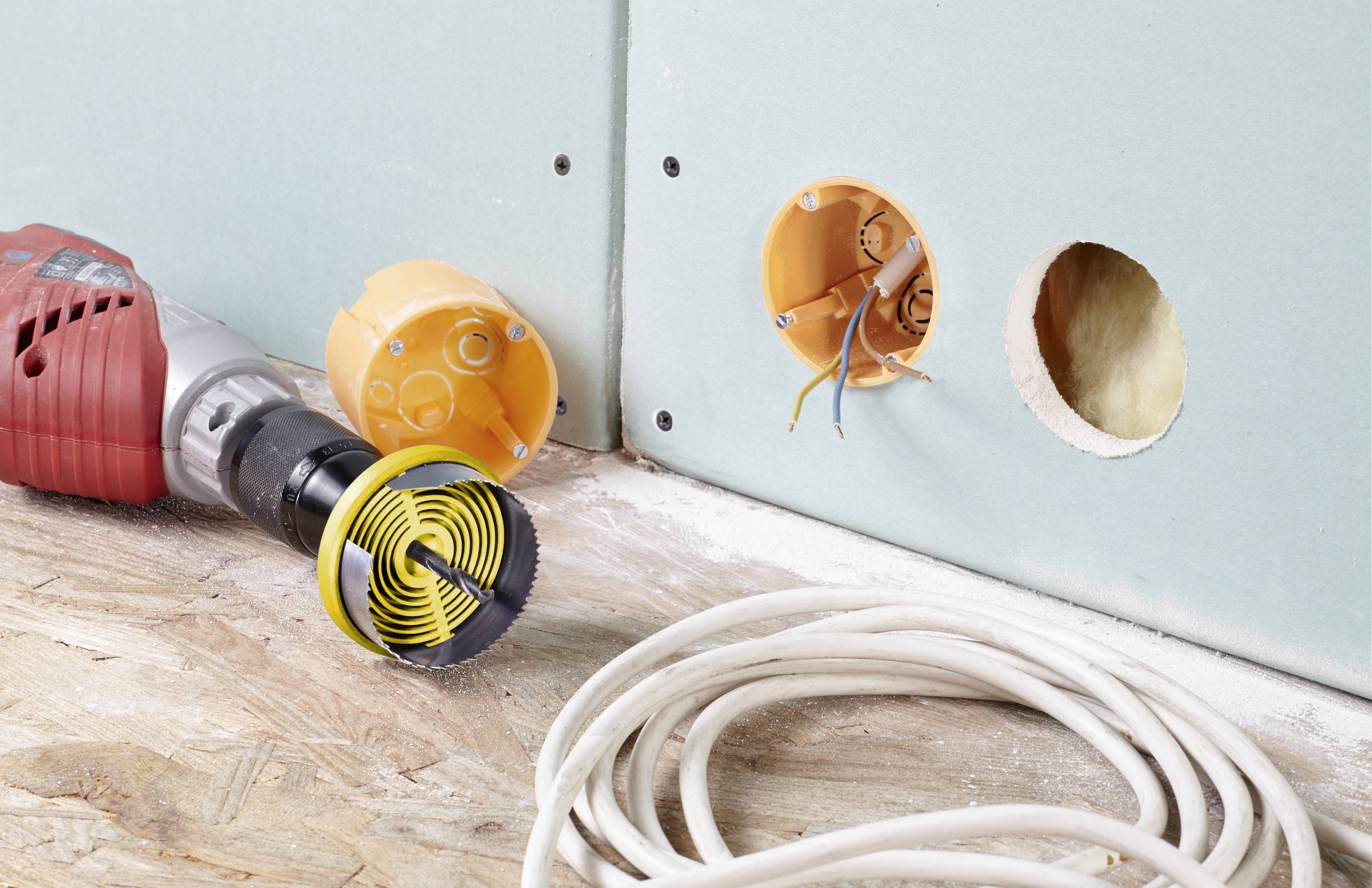 Gradbišče z mavčno ploščo, vrtalnim strojem, dvema priključenima kabloma in kolutom kablov. Električna instalacija v teku.