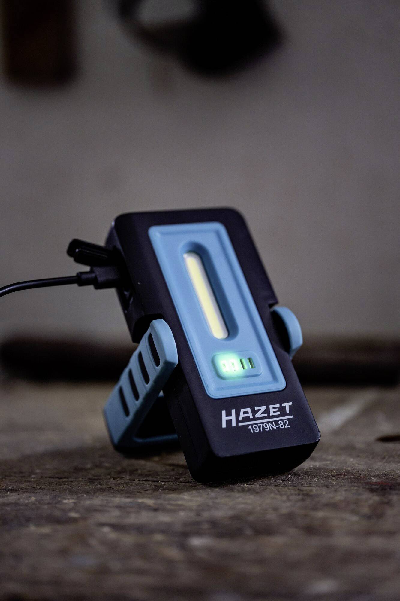 Prenosna LED delovna svetilka znamke Hazet na mizi, priključena na polnilni kabel.