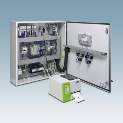 'Odprt električni razdelilnik z elektronskimi komponentami in kabli, ob njem tiskalnik z natisnjeno nalepko v pisarni.'