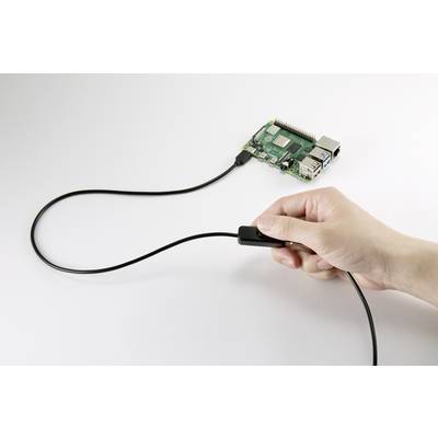 Roka drži kabel, ki je priključen na Raspberry Pi. Raspberry Pi leži na mizi in je povezan s kablom.