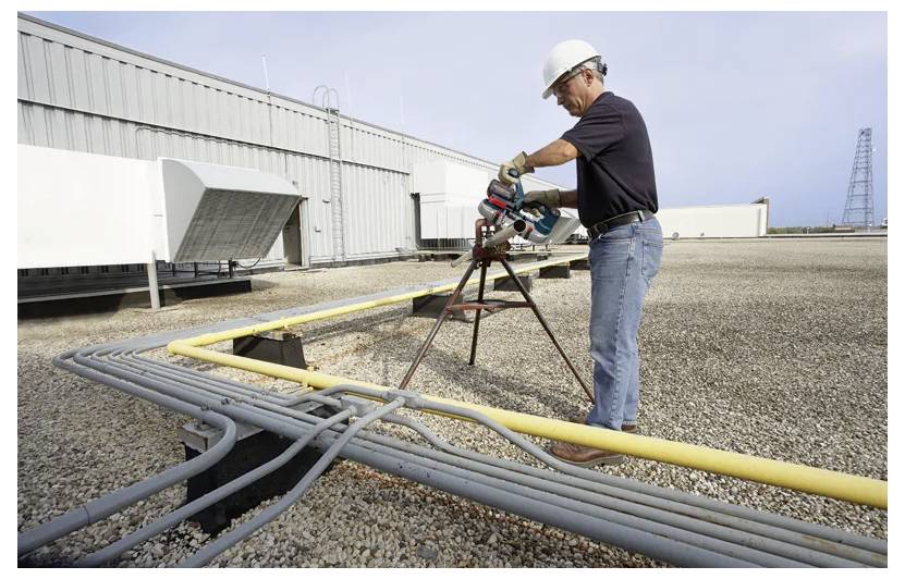 Delavec na gradbiščih vrta konduit skozi snop strešnih cevi ob industrijski stavbi.