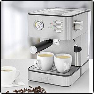 Srebrni espresso aparat z dvema belima kavnima skodelicama na mizi. Zraven ležijo kavna zrna in še ena prazna skodelica.