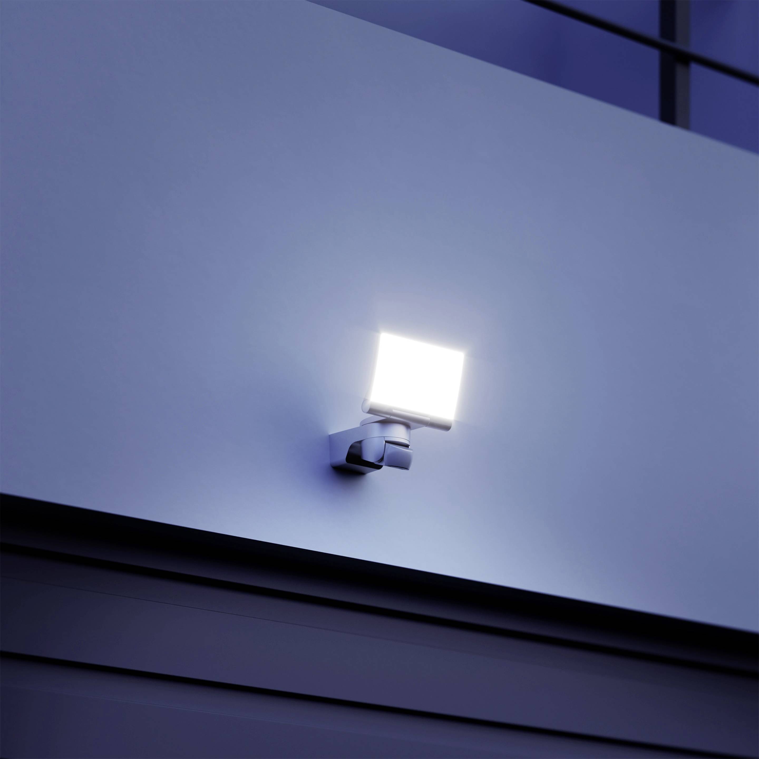 Svetilka zunanjega reflektorja je nameščena na sivi steni in razsvetljuje prostor pod njo.