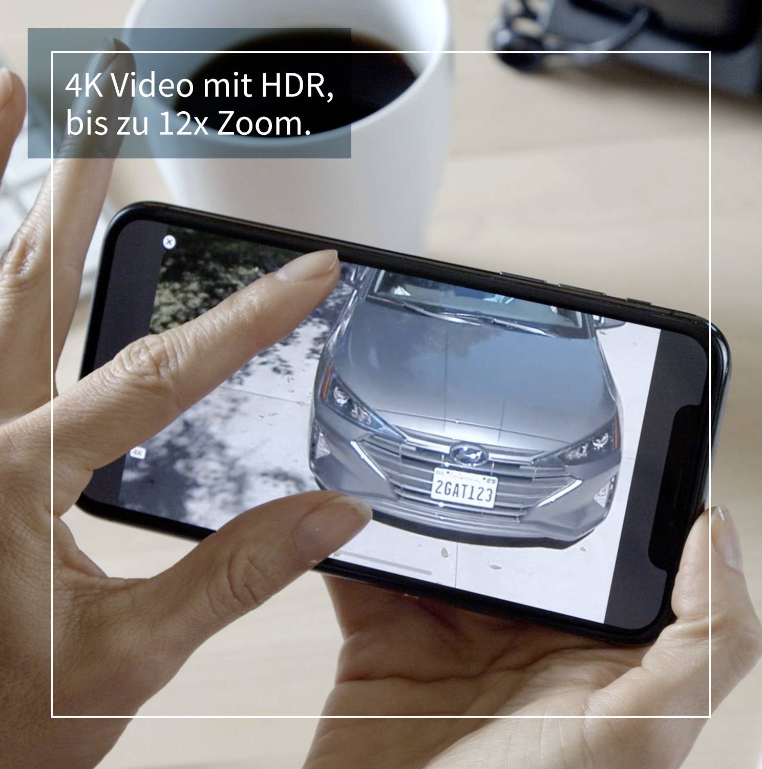 Oseba drži pametni telefon in prikazuje sliko avtomobila. Besedilo zgoraj levo: '4K video z HDR, do 12x zoom.' V ozadju skodelica kave.