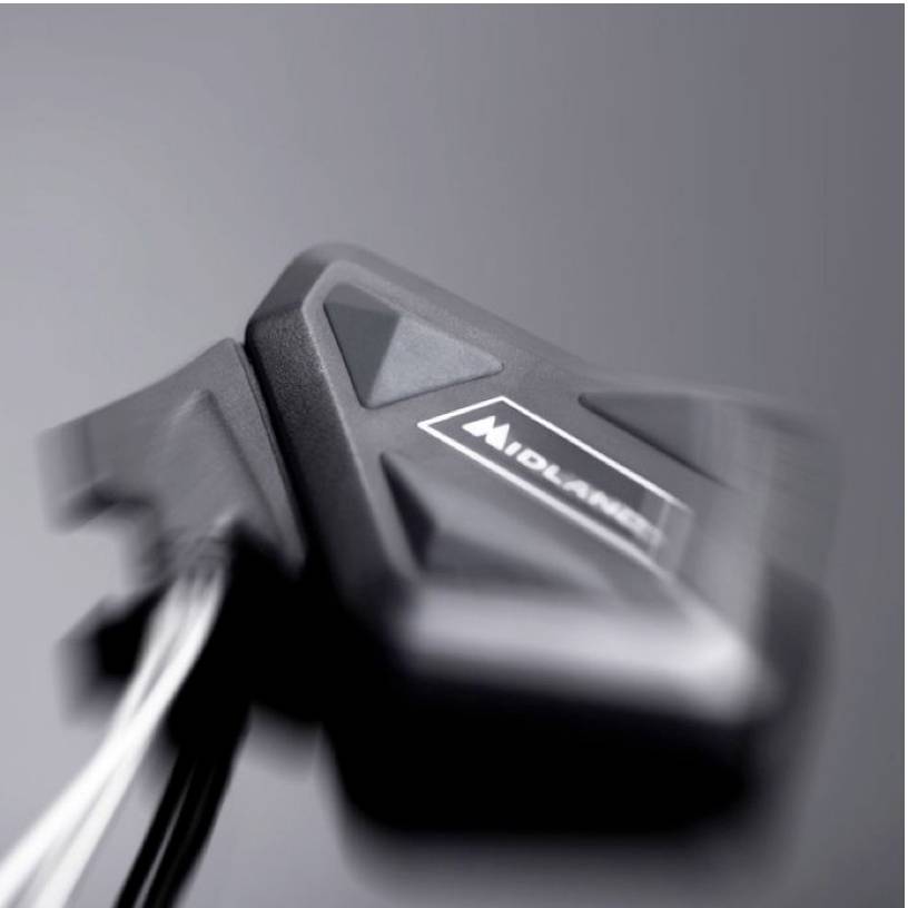 Črna naprava z logotipom 'Midland' in več kabli, nejasno prikazana v ospredju pred sivo podlago.