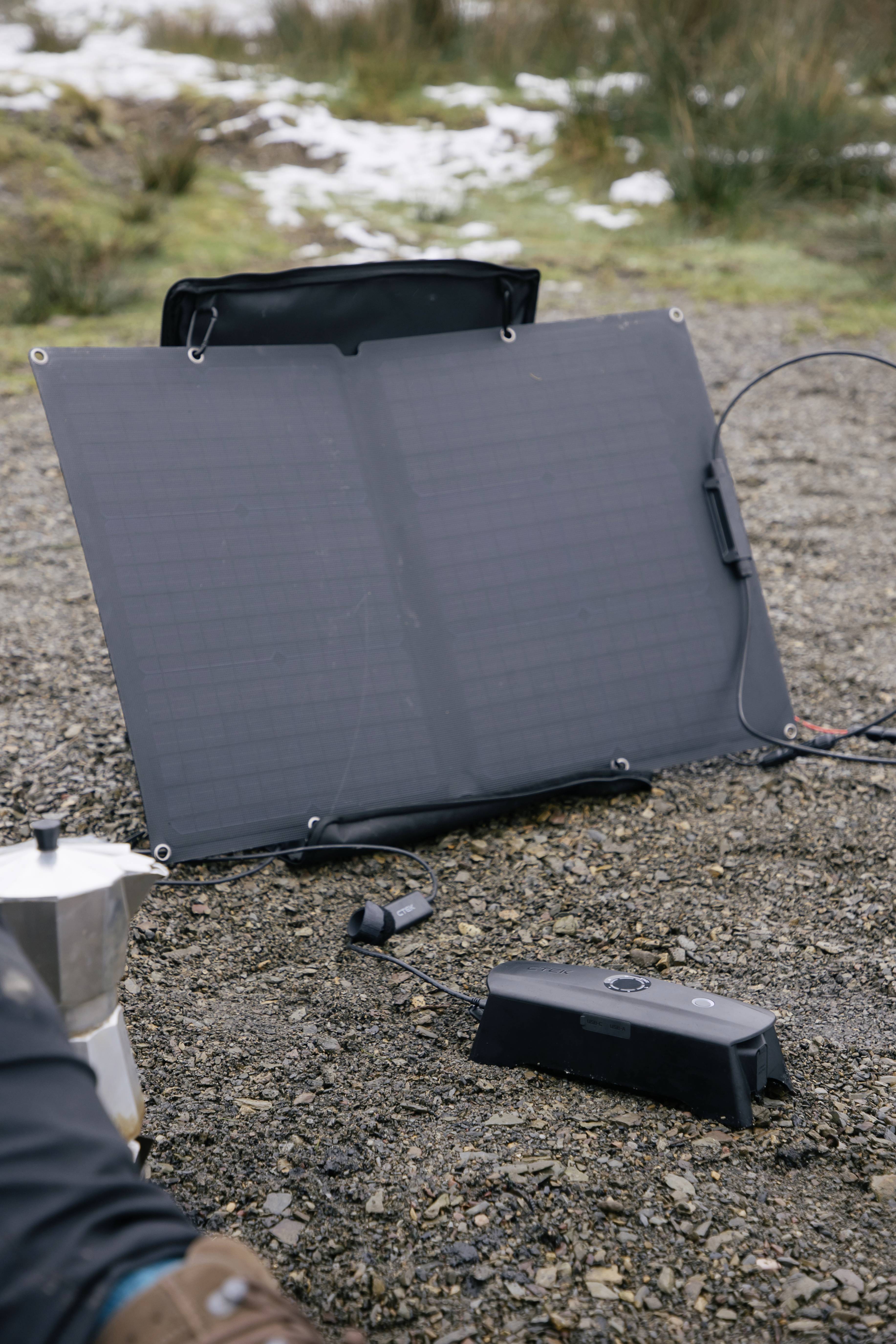 Prenosljiv solarni panel na kamnitem terenu, postavljen na prostem poleg kavnega aparata in elektronske naprave.