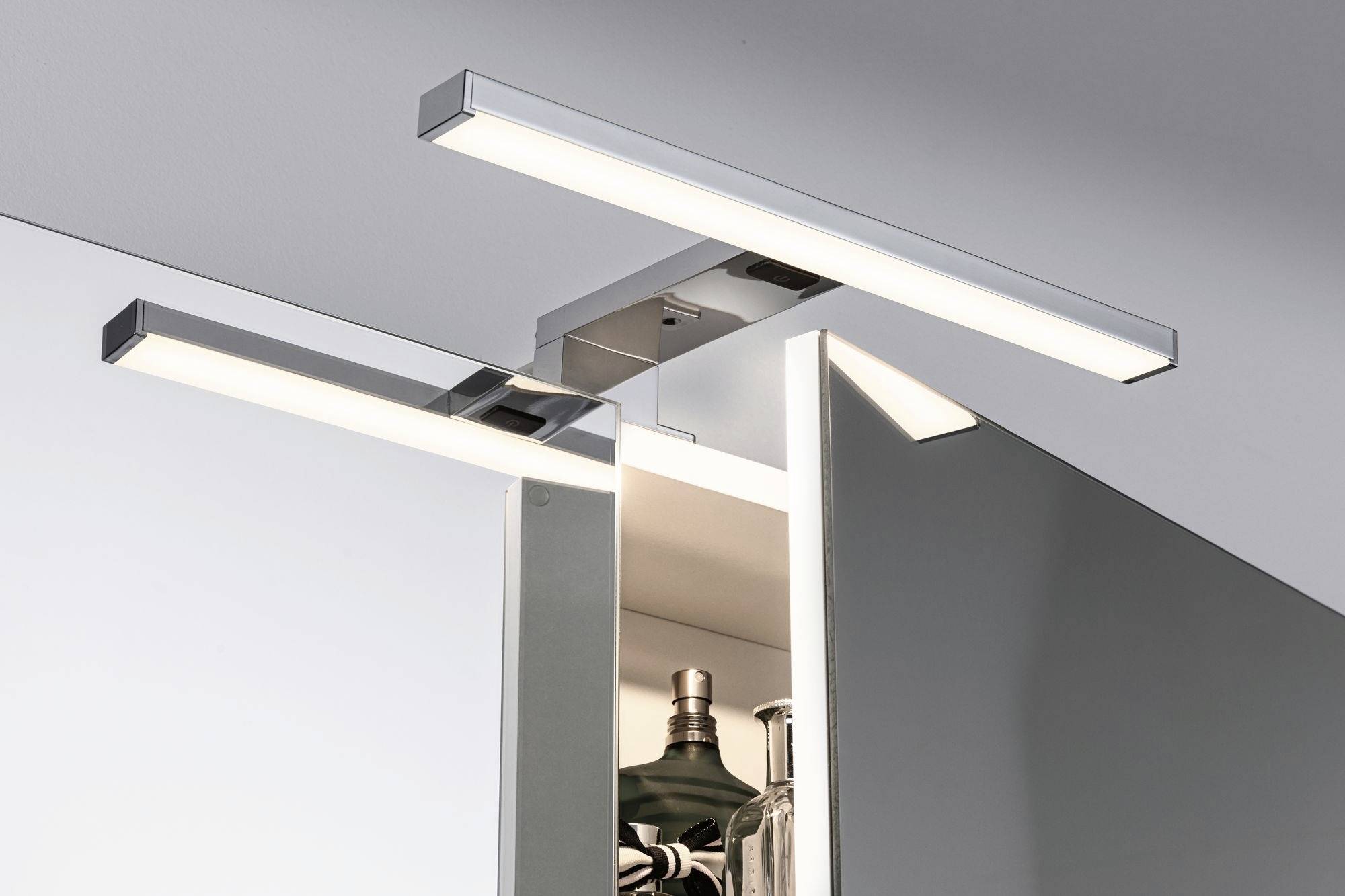 Sodobna LED-luč nad odprtim kopalniškim ogledalom, ki prikazuje toaletne pripomočke. Elegantno, minimalistično oblikovanje.