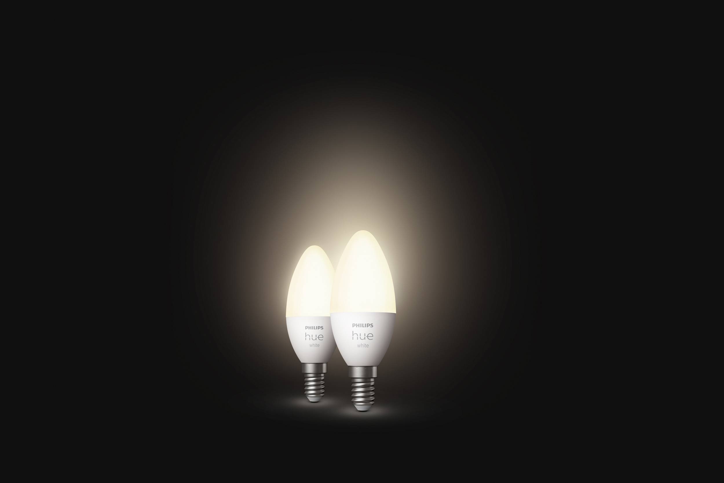 Dve svetleči žarnici na temnem ozadju z blagovno znamko 'Philips Hue'. Sta prižgani in oddajata toplo svetlobo.