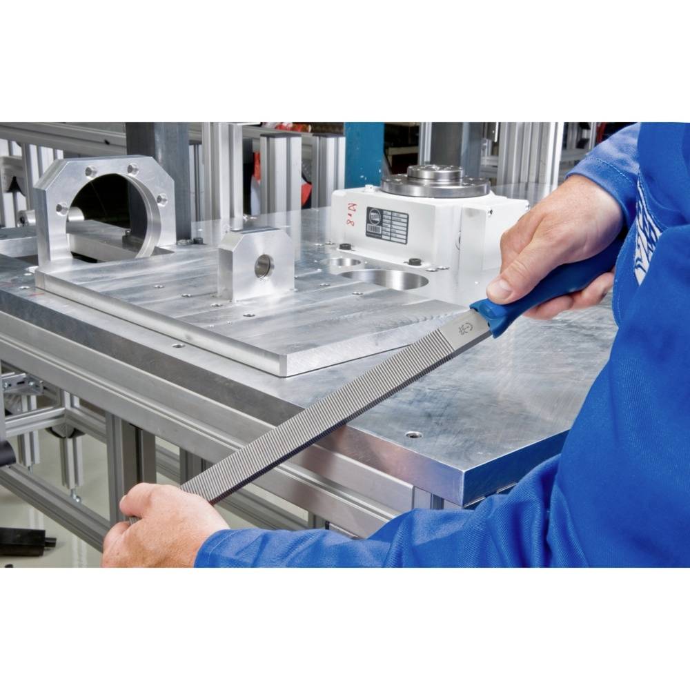 Obrtnik uporablja pilo za obdelavo kovine na delovni mizi. V ozadju so vidni strojni deli.