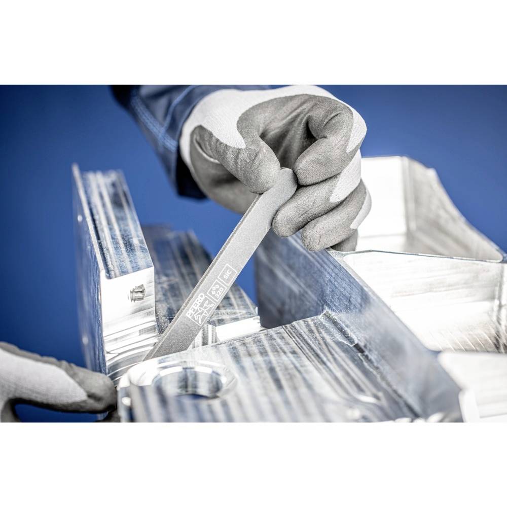 Oseba nosi rokavice in z datekom poravnava rob kovine na delovni mizi, da bi jo zgladil.