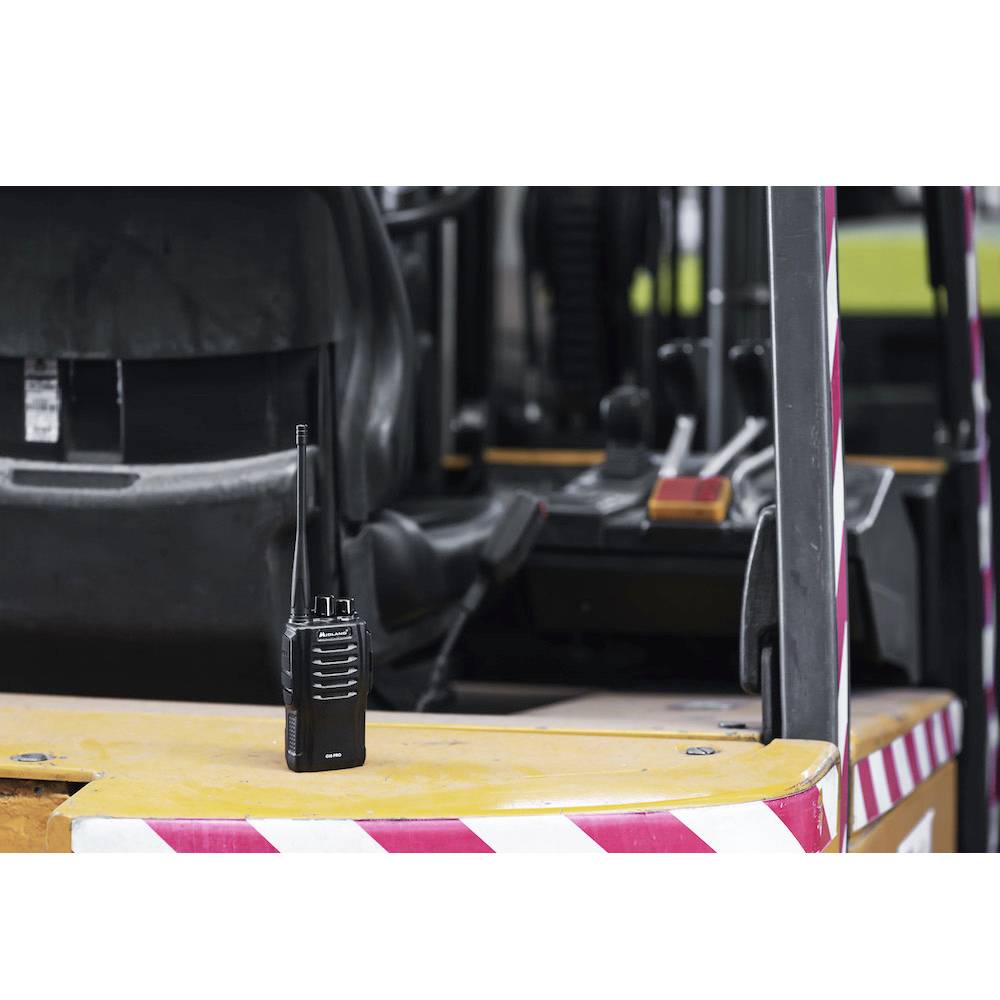 Na armaturni plošči rumene vozilo z vzorcem prog stoji walkie-talkie, v ozadju so vidni upravljalni elementi.
